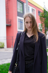 Fototapeta premium portrait of confident attractive brunette woman in black on background of colorful bright buildings. business woman. feminine. millennial people