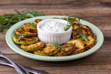 Fried slices of zucchini with sour cream sauce. Courgettes with herb for dinner on natural wooden background