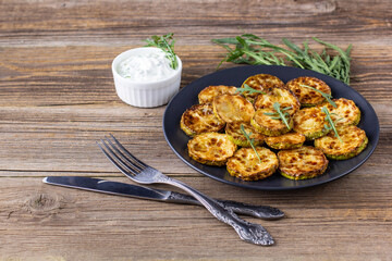 Fried slices of zucchini with sour cream sauce. Courgettes with herb for dinner on natural wooden background