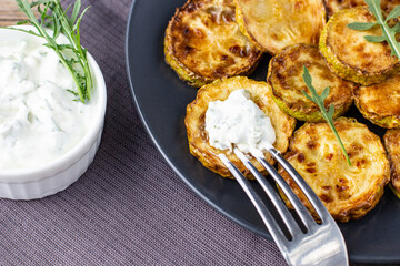 Fried slices of zucchini with sour cream sauce. Courgettes with herb for dinner on natural wooden background
