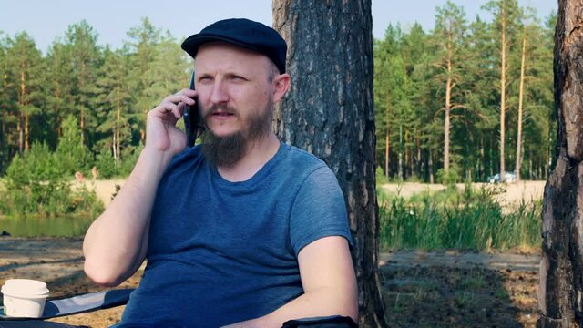 A man is resting in a forest in a unique place in an ecologically clean area. No hustle and bustle. During the rest he talks on the phone. Camping in a national park for a family vacation.