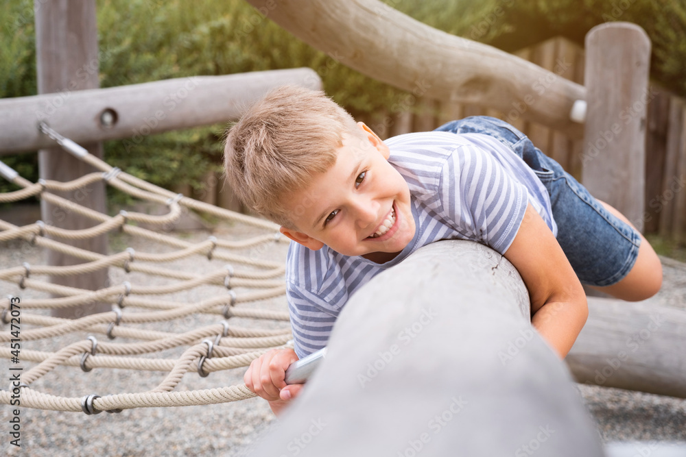 Wall mural Cheerful and mischievous boy having fun at wooden playground outdoors.