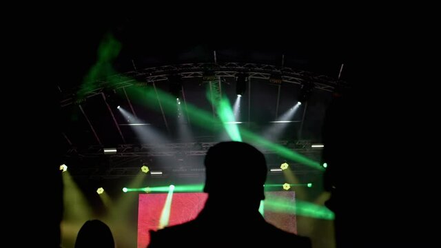 Silhouettes of People at Night at a Rock Concert. Stage lighting with spotlights, background. Flickering light. Open scene. Stage Lighting spotlights. Smoke in crowd. Close up. Slow motion.