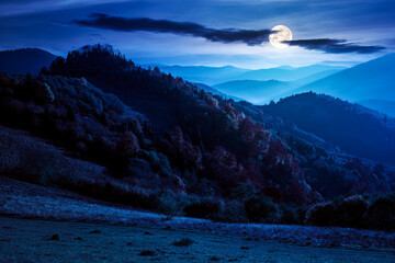 mountain scenery in autumn at night. forest in colorful foliage on the hills. distant range beneath...