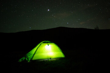 Yellow tent at night in the mountains against the background of the starry sky