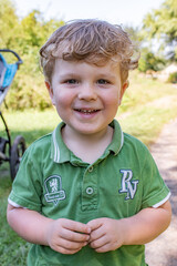 Trzyletni chłopiec w zielonej koszulce polo uśmiechający się na tle łąki - obrazy, fototapety, plakaty