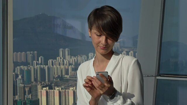 Pretty businesswoman using smart phone in high-rise modern office.