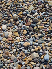 A full frame of many, many pebbles and rocks deposited on a beach and forming an abstract near-mosaic under the influence of the sea and tide.