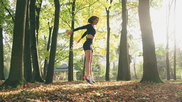 Fit young woman with short haircut training legs with squats and jumps at local park. Beautiful female athlete in activewear doing sport activity outdoors.