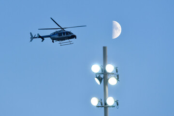 Police helicopter, stadium jupiters and moon on the dusk blue sky - Powered by Adobe