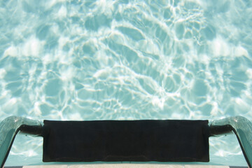 Top view of swimming pool with clear blue water and metal ladder close-up.

