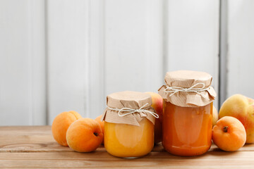 Two jars with peach jam and fresh fruits on wooden table.