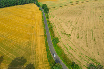 Wąska, wiejska asfaltowa droga przebiegająca przez pola uprawne. Widok z drona.