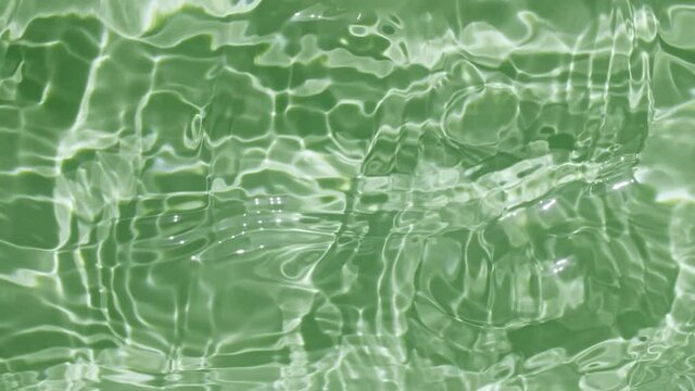 Water splash green colored. Pure water with reflections sunlight in slow motion. Sun and shadows. Motion clean swimming pool ripples and wave. 4k. High quality 4k footage