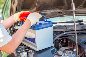 Maintenance of the machine. A male car mechanic takes out a battery from under the hood of a auto...