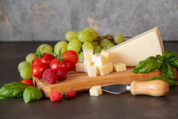 tomatoes, cheese, basil, raspberries and grapes on an olive board on a dark background