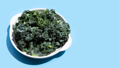 Kale leaves in white bowl on blue background.