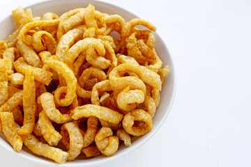 Fried crispy pork rinds in white bowl on white background.