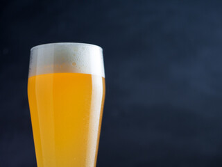 A glass of wheat beer in a tall glass on a dark background