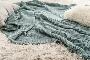 Knitted plaid with pillows on carpet