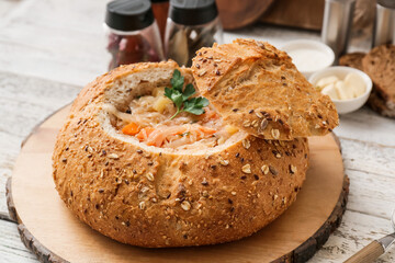Board with tasty sauerkraut soup served in fresh bread on light wooden background