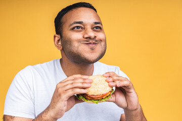 Young african american indian black man eating hamburger isolated over yellow background. Diet concept.