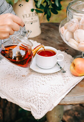 Woman pouring tea on a cup from glass teapot  outdoor on the table.