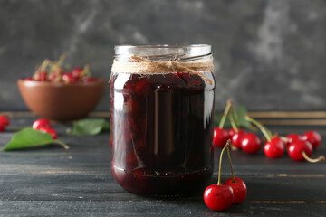 Jar with tasty cherry jam on dark background