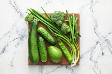 Board with different green vegetables on light background