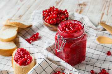 Composition with jar of red currant jam and sandwich on light wooden background, closeup