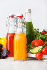 Bottles with healthy juice, fruits and vegetables on light background