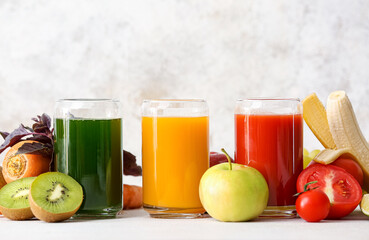Glasses with healthy juice, fruits and vegetables on light background