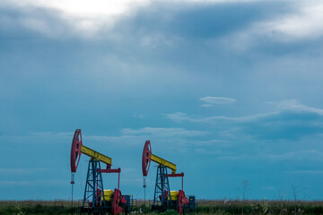 Fototapeta na wymiar pumpjacks operating at an oil well in field under cloudy sky