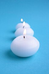 Fototapeta na wymiar Close-Up of three white illuminated candles against blue background.