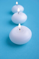 Close-Up of three white illuminated candles against blue background.