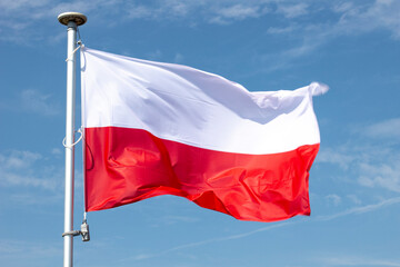 Polish flag on a background of the cloudy sky. National symbol of Poland on the mast.