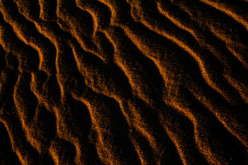 Sand texture outlined by the wind. Wavy shapes of light and shadow.