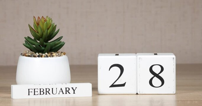 Wooden calendar with an important event for february 28, a woman's hand sets the date on the calendar. Winter season.