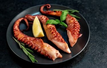grilled octopus tentacles, on a dark plate on a stone background