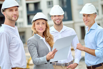 Confident building inspector with a document and builders looking ahead
