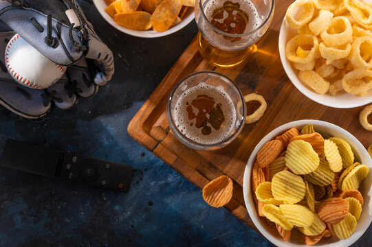 Two glasses of beer, chips, snacks. Baseball glove. View from above. High angle view. Relaxation with friends, watching sports games on TV.Color image. There are no people in the photo.