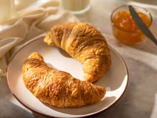 Two croissants on a plate. Close-up. In the background, orange jam and milk. Traditional French breakfast. High angle view. Hotel, cafe, bakery, restaurant. Advertising, banner, poster.