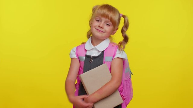 Little blonde child kid girl in school uniform showing biceps and looking confident, feeling power strength for study, energy to gain success win. Yellow studio background. Back to school. Childhood