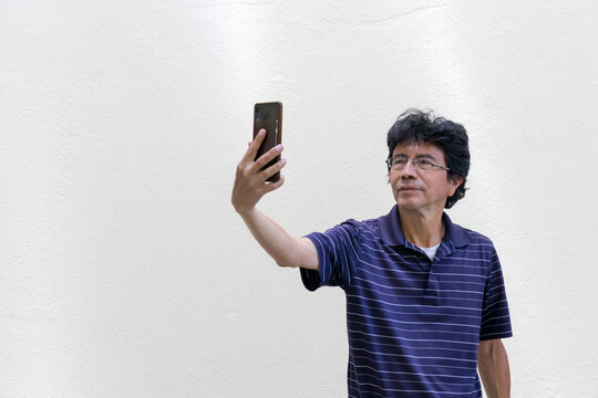 Hispanic man taking a selfie with cellphone on a white background