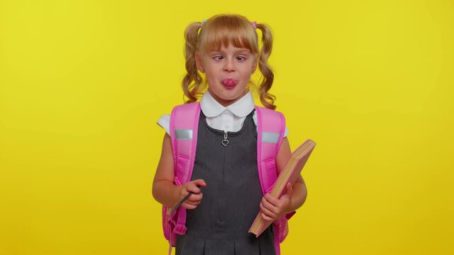 Smiling cute funny girl in school uniform, making humorous face with eyes crossed, playing fool, having fun with stupid brainless dumb expression over yellow studio background. Back to school concept