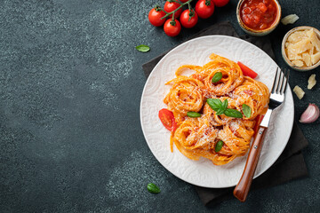 Tasty appetizing classic italian tagliatelle pasta with tomato sauce, cheese parmesan and basil on plate on dark table. View from above, horizontal. Top view with copy space