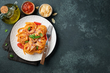 Tasty appetizing classic italian tagliatelle pasta with tomato sauce, cheese parmesan and basil on plate on dark table. View from above, horizontal. Top view with copy space