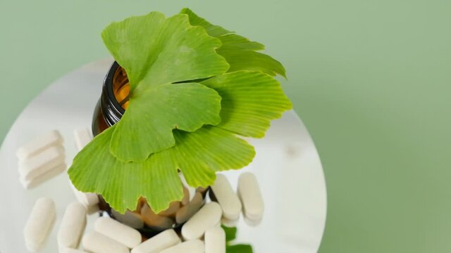 Ginkgo biloba tablets.Alternative medicine and homeopathy. glass jar with pills and ginkgo biloba leaves on a green background. Rotation. High quality 4k footage
