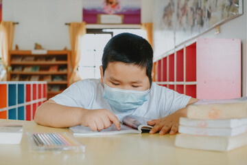 Asian little boy with face mask reading a book at school, Close up...
