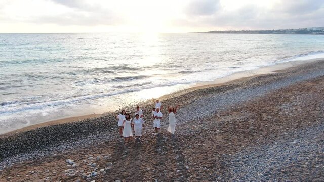 Zoom Out Of Group Of Multigenerational Asian Family Waving Smiling Standing At Sunset On Picturesque Mediterranean Sea Shore. Gorgeous Landscape At Subtropical Tourist Resort With Happy People Resting